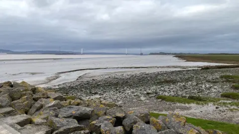 Pete Simson/BBC The Severn Estuary showing rocks in the foreground and the original Severn Bridge in the background