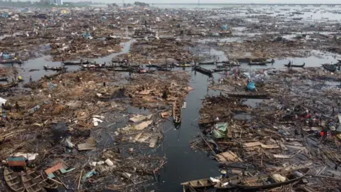 Gift Ufuoma/BBC Wooden debris and boats in Lagos Lagoon with Third Mainland Bridge in the distance.