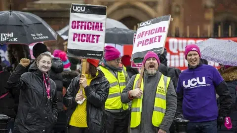 Anggota PA Media Union, dua di antaranya dengan rompi kuning tinggi di garis piket selama aksi mogok sebelumnya. Dua dari mereka memegang tanda -tanda yang mengatakan 'piket resmi' sementara yang ketiga mengenakan atasan UCU biru.