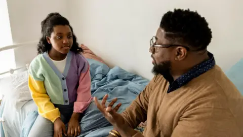 Getty Images Father and daughter discussing while sitting on bed at home 