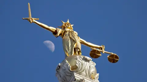 Brass statue of lady justice, against a blue sky