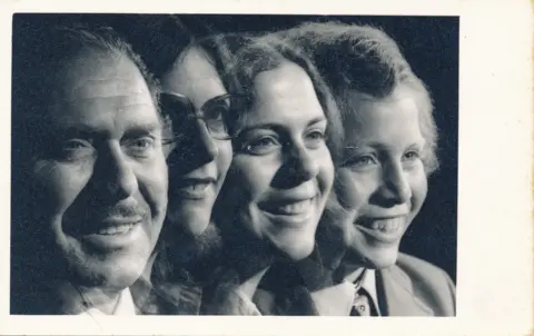 The Leibowitz family A studio photograph of four people – a man, woman, girl and boy – smiling. It's in black and white