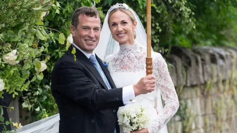 Peter Phillips holds up an umbrella in his wedding suit next to his wife Harriet Sperling, who is in a lacy wedding dress