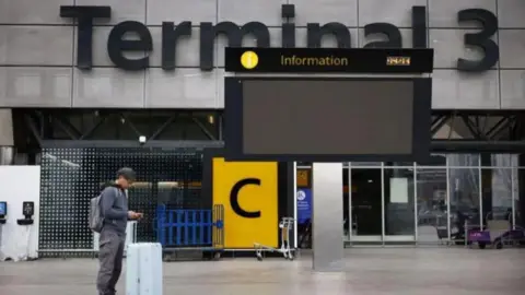 EPA A man standing outside a deserted Terminal 3 at Heathrow. He is wearing dark coloured clothing and has a white suitcase. 