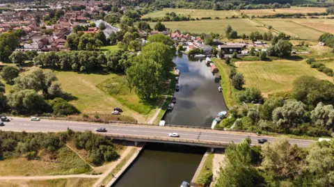 Drone image of the A146 bridge over the River Waveney in Beccles, showing cars on bridge, moored boats on river and surrounding green space and housing