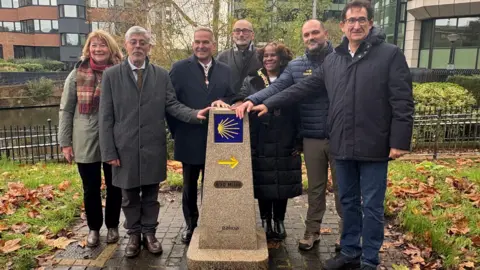 A group of seven people standing next to the granite marker.