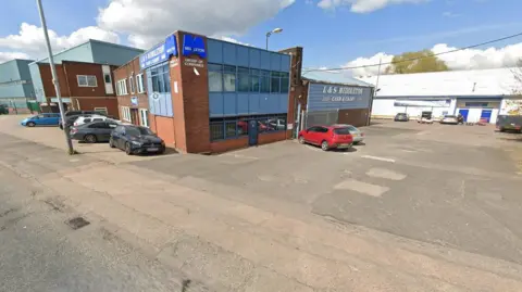Various buildings are in the background, in this generic image of buildings. Vehicles are parked in front of some of the buildings. 