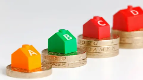 Four stacks of pound coins with small toy houses on them labelled A, B, C and D 