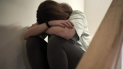 Getty Images An anonymous woman holds her head in her hands