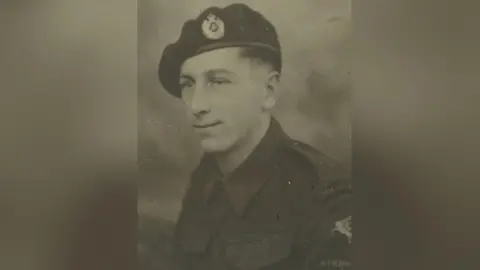 A black and white photograph of a young man in army uniform. He has short dark hair and a beret. 