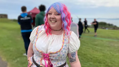 Steph Randalsome has fluorescent dyed hair and is dressed up as a medieval-serving wench, wearing a floral bodice and choker.