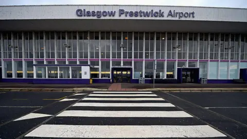 Getty Images The entrance to a large airport building, with the view coming from across the street. The sign says Glasgow Prestwick Airport