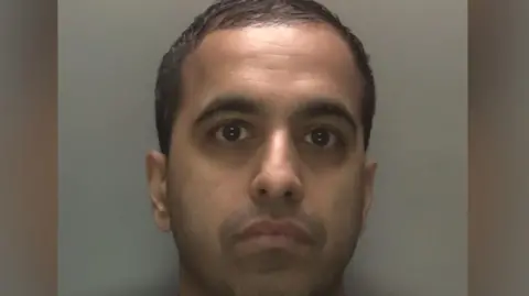 An image of a man in a red top in front of a grey background
