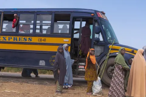 Ayo Bello / BBC Pessoas descem de um grande ônibus.