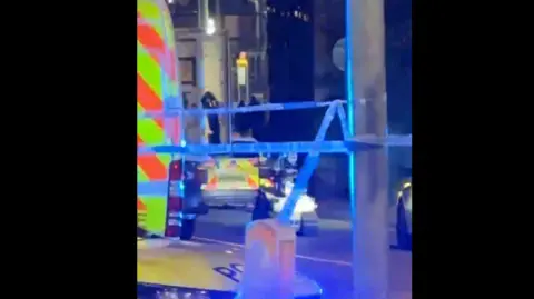 Josh Upton A bomb squad robot is seen moving towards a bus, alongside a police van in an area covered in police tape.