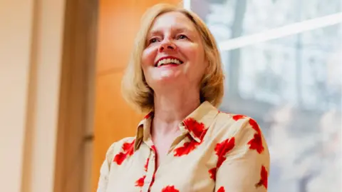 Theresa McDermott Theresa McDermott is standing outside a building wearing a shirt with red flowers on it. She has shoulder length, blonde hair and is smiling while looking slightly above the camera.