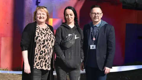 Leeds City Council Councillor Debra Coupar, artist Harriet Wood and Simon Hodgson, head of Safer Leeds, standing in front of the mural