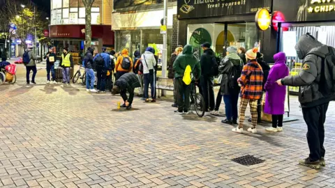 Street view of people lining up to collect warm meals
