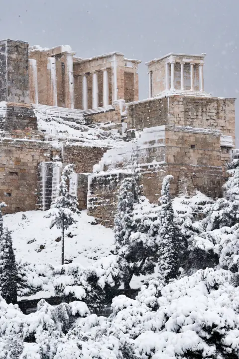 Milos Bicanski / Getty Images Snow falls on ancient ruins in Athens