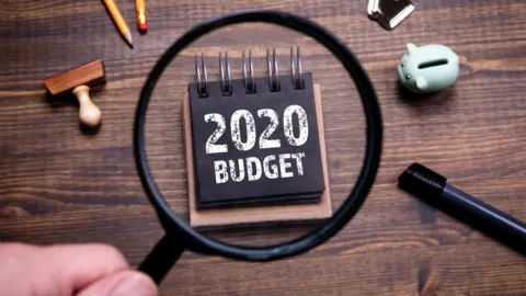 Getty Images Magnifying glass over budget block