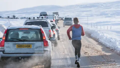 Liam Anderstrem / Airborne Lens Man running along road at Glencoe