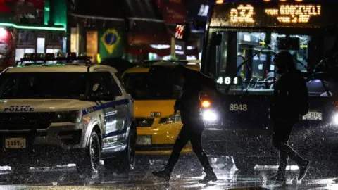 Getty Images Rain falls as pedestrians walk on a street in Queens, New York City, January 9, 2024.