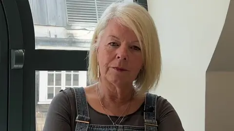 BBC Mrs O'Sullivan, a woman with blonde hair wearing a dark top and denim dungarees
