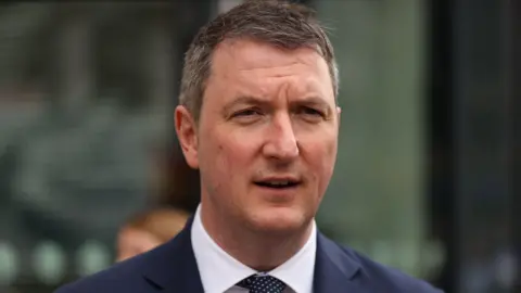 PA Media John Finucane. He has short brown hair, wearing a navy blazer, white shirt and navy polka dot tie.