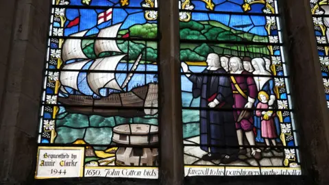 Karl Bird / BBC A stained glass window inside a church. It shows an image of a group of people waving to a ship that is setting sail. 