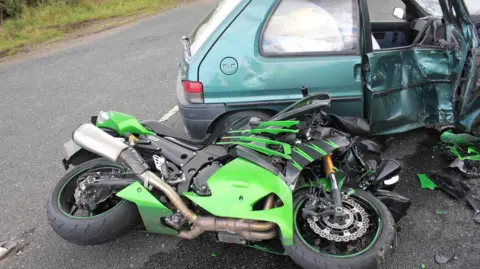 Gordon Castle A badly mangled motorbike is stuck under a car which is also badly damaged.