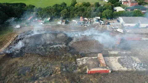 Environment Agency An aerial view of the site showing smoking piles of rubbish with shipping containers and other structures 