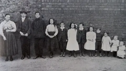 University of Cambridge An Edwardian family showing a mother with 11 children in order of age standing against a brick wall