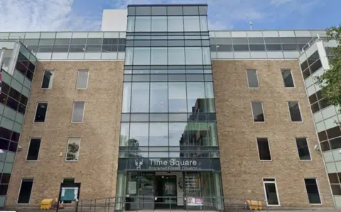 Bracknell Forest Council's building. It has all glass windows at the centre of the building which protrudes the rest of the sandy-coloured brick frontage. there is a sign above the door on the glass that reads Time Square Bracknell Forest Council