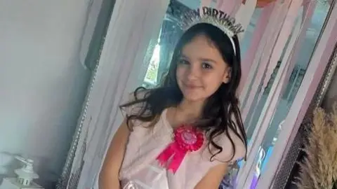 Aria Thorpe is wearing a tiara which has "happy birthday" written on it. She is wearing a pink dress and has a pink birthday badge on.