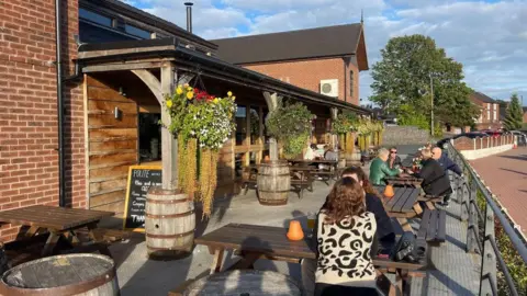 Six people are on benches outside. A pavement is to the right on the photo.