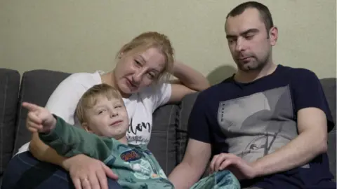 Svitlana, Dima dan putra mereka yang berusia empat tahun, Vova, duduk di sofa mereka.
