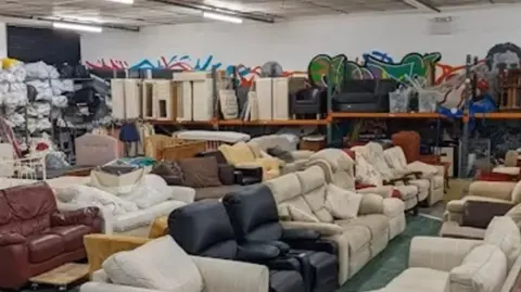 Shrewsbury Furniture Scheme A room filled with sofas of different types and shelves holding other items at the back of the room
