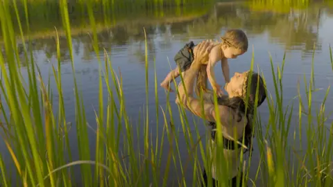A woman holding a baby by the Doongmabulla Springs
