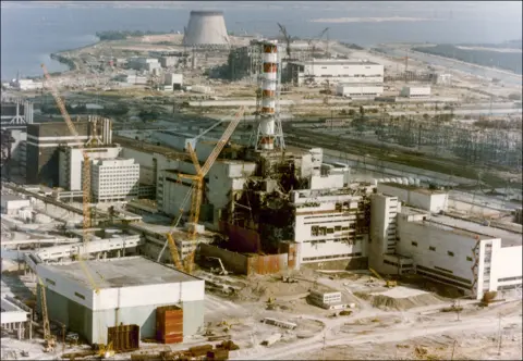 SHONE/GAMMA/Gamma-Rapho via Getty Images View of the Chernobyl Nuclear Power Plant on 29 April 1986, three days after the explosion. The building housing reactor four is badly damaged, with blackened debris below a red and white chimney.