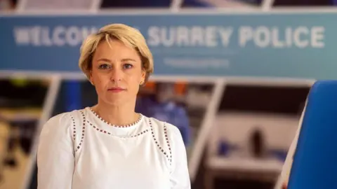 A woman with short blonde hair, wearing a white shirt, looking at the camera. 