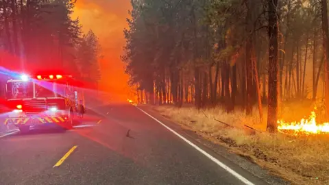 EPA/Shutterstock A Spokane Valley Fire Department truck on the road, surrounded by burning trees 