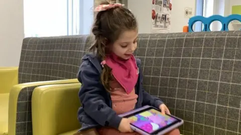 Family Flory playing on an iPad. She is watching Peppa Pig on a sofa.