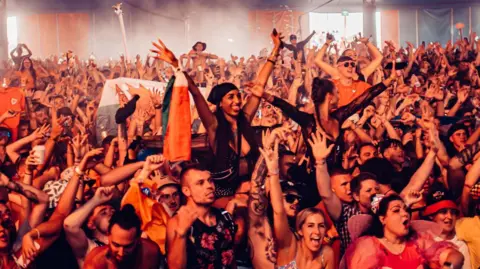 Creamfields A large crowd of people at Creamfields are facing a stage with their arms in the air. 