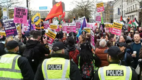 Getty Images Three police officers in yellow hi-vis jackets stand in front of a rally of counter-protesters holding placards with messages opposing Britain First. The placards show support for LGBT+ people and refugees and have message such as "smash the far right" and "refugees welcome, stop the far right". There are some Palestinian flags. Old buildings with shops are in the background.