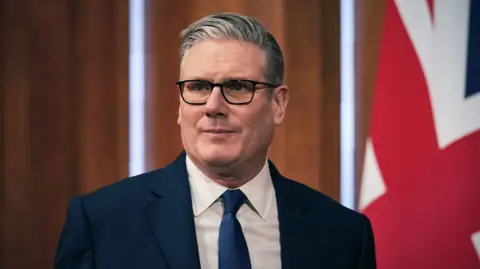 Keir Starmer looks to the left of frame while wearing a dark suit and tie against the Union flag during a press conference in the downing Street Briefing Room in London on 1 April.
