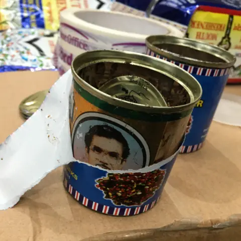 Border Force Two tins with blue wrappers sit on top of a cardboard box. The tins are missing their lids.