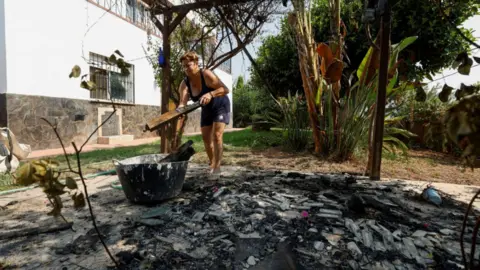 Reuters A woman in a black tank top and shorts cleans up burned out wood from a garden patio 