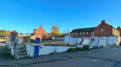 The site of a demolished factory in Ringstead, showing large metal fencing around piles of bricks