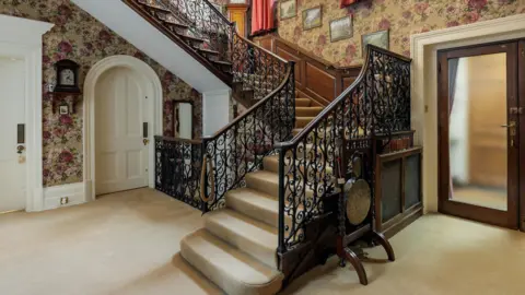 Savills An ornate staircase in a large room with flower pattern wallpaper