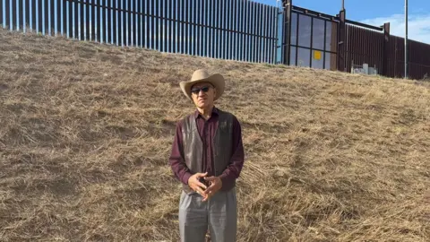 Man in cowboy hat in front of detention wall